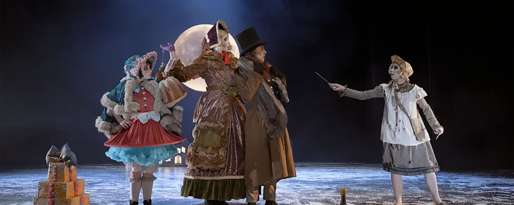On a snowy winter night, three dancers, the Donnarumma family stand together looking to the right at the little match girl who is wearing a white bonnet and pinafore and is holding out a match.