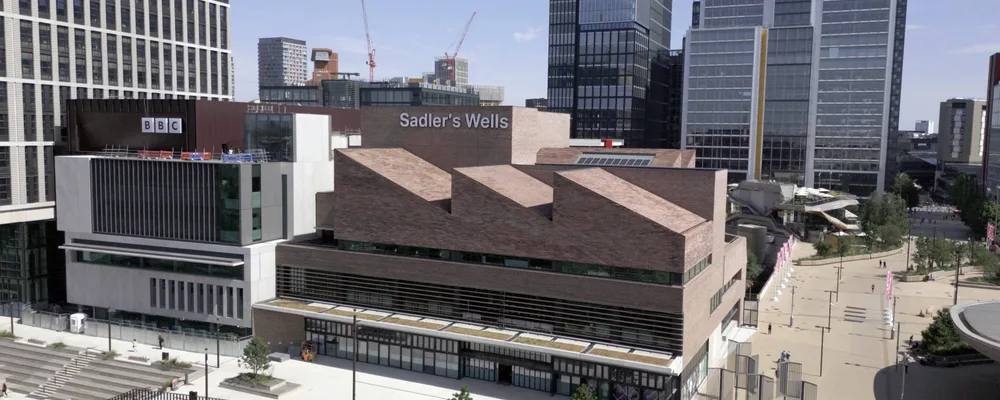 Aerial view of a modern urban area featuring multi-story buildings and the Sadler's Wells Theatre at the center, with pedestrian pathways and greenery.