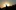 The silhouette of a woman standing on a hill with her arms raised, the sun sets behind her