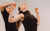 Two dancers in black raise their arms, facing different directions.