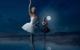 A ballet dancer in a white tutu and a ballet dancer in a black tutu float en pointe on the surface of a lake