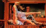 Two performers on stage, one lying on a table supporting the other arched
